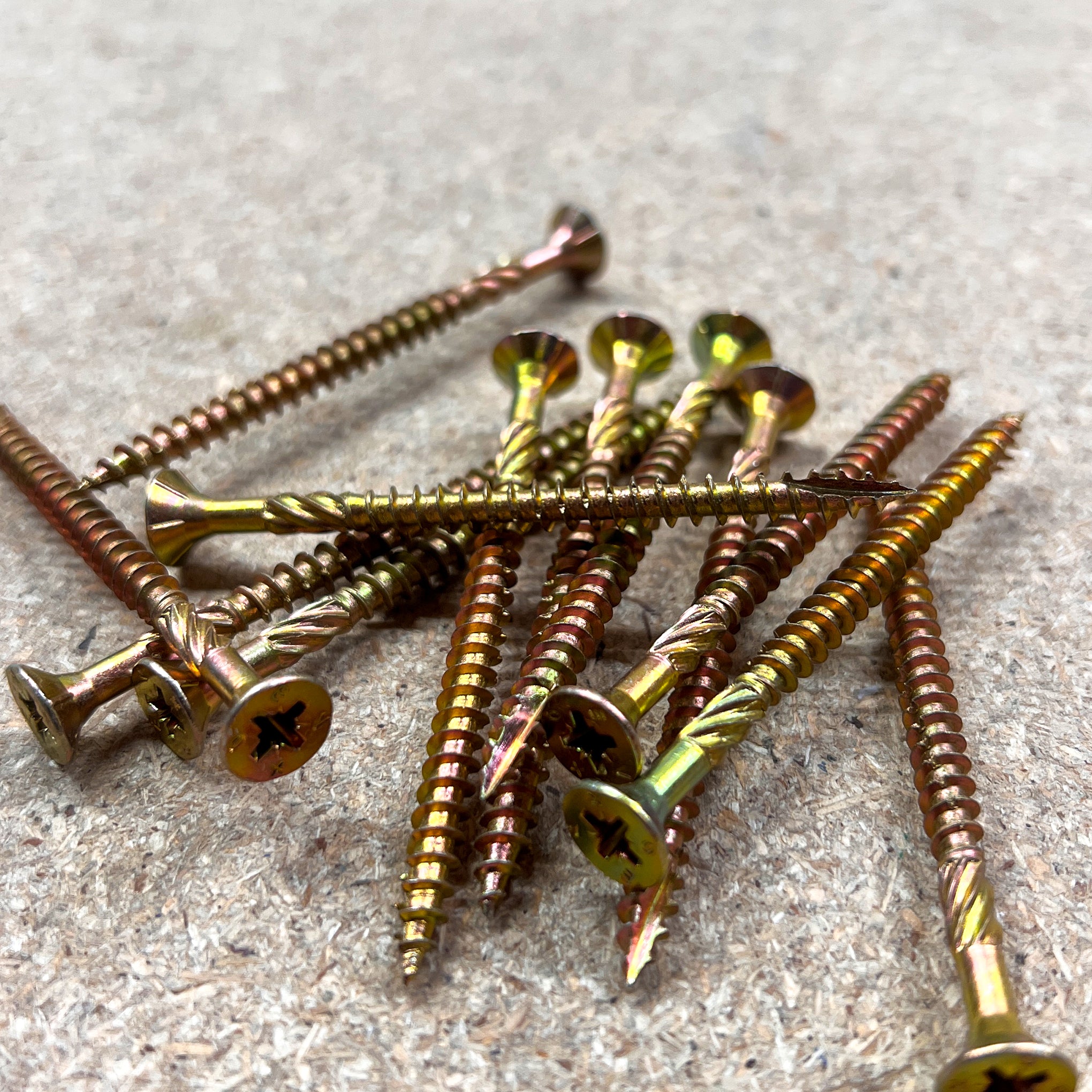 An image of Yellow Zinc Pozi Wood Screw Scattered Across Chipboard